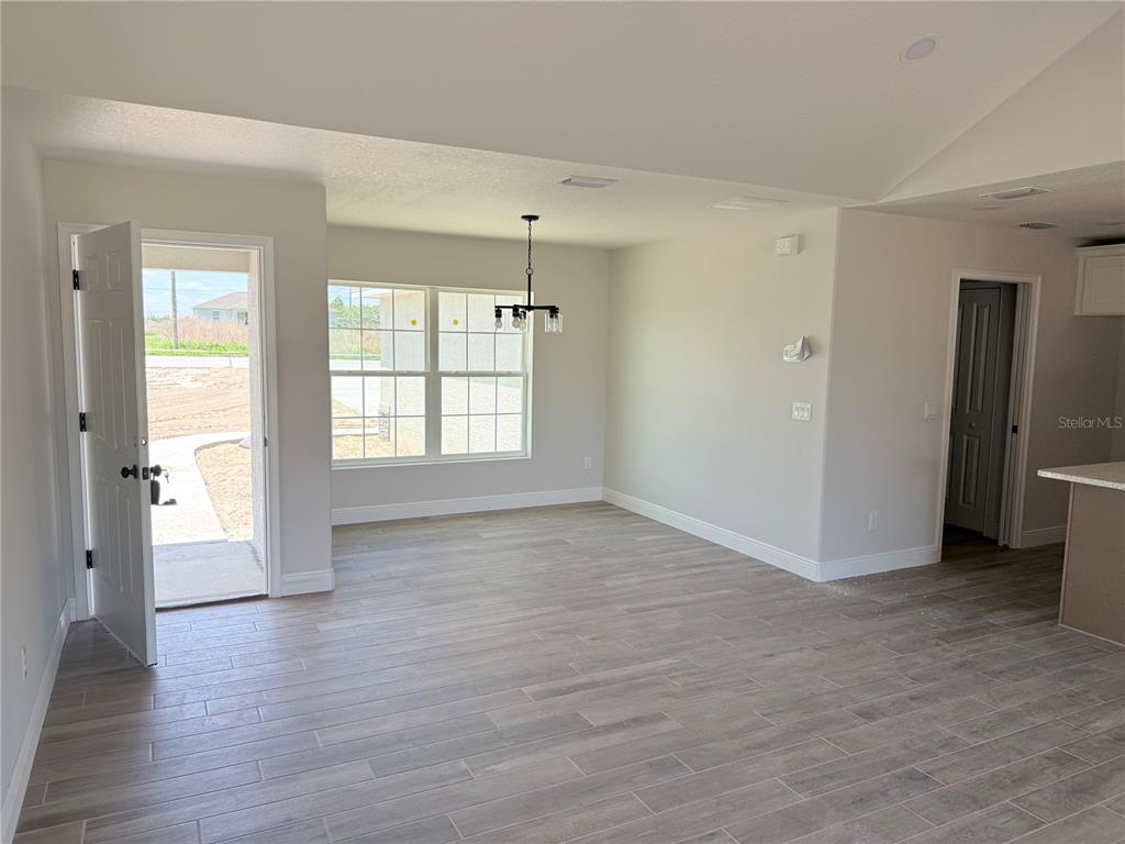 A dining area with wood-look tile flooring, a modern chandelier, and an open exterior door — 133 LARCH ROAD, OCALA, FL