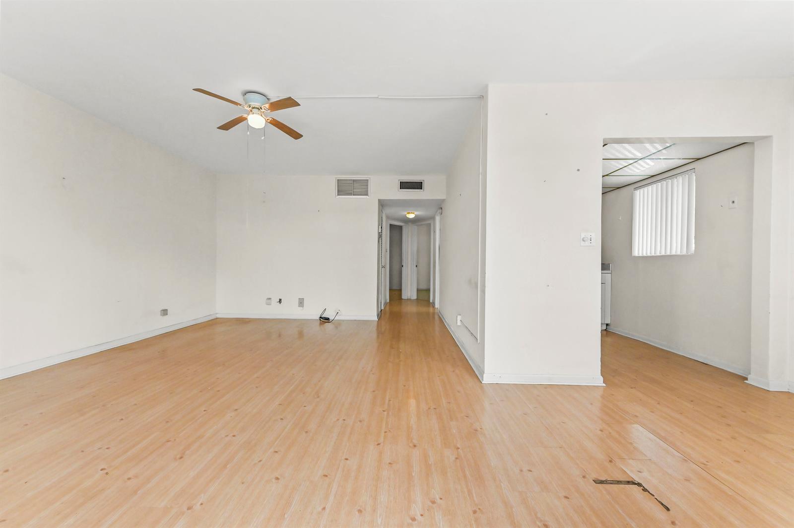 An empty living room features light wood-look flooring, a ceiling fan, and an adjacent kitchen — 1950 Lake Osborne Drive # 9, FL 33461, FL