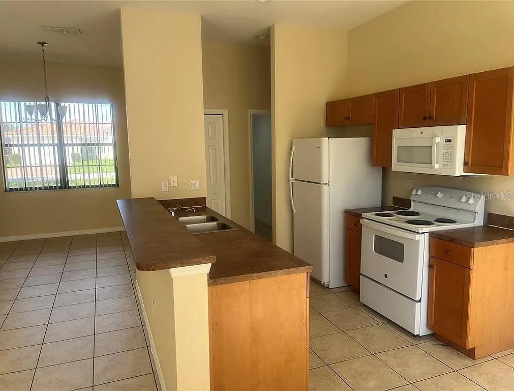 A kitchen features wood cabinets, white appliances, a breakfast bar, and tile flooring — 404 CINNAMON DRIVE, KISSIMMEE, FL