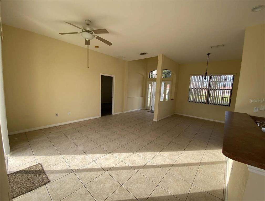 An open-concept living area features beige walls, tile flooring, a ceiling fan, and large windows — 404 CINNAMON DRIVE, KISSIMMEE, FL