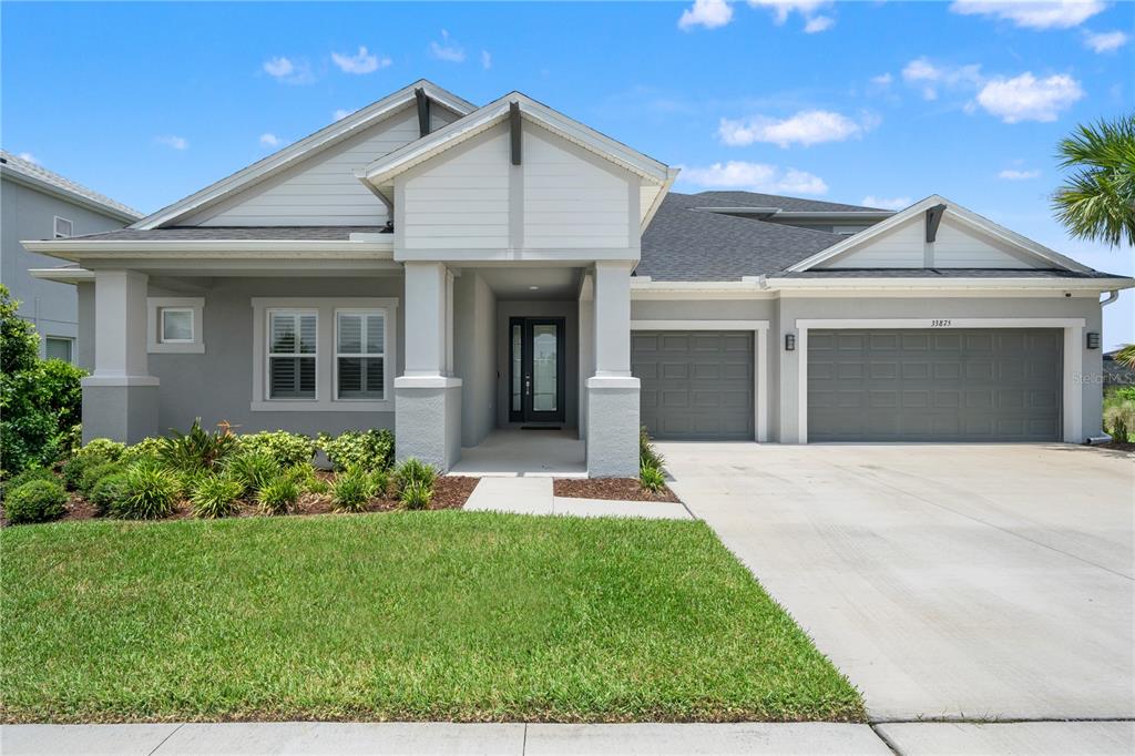 A single-story house with a gray exterior, a three-car garage, and a covered front porch — 33875 CASTAWAY LOOP, WESLEY CHAPEL, FL