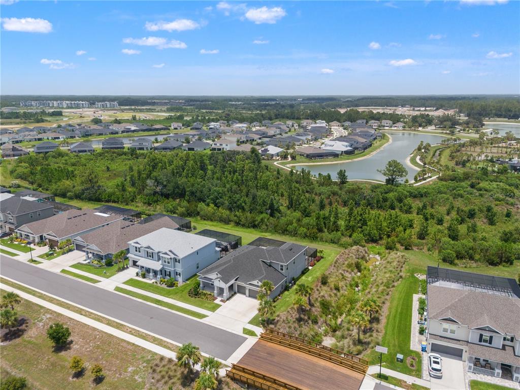 An aerial view shows suburban houses with screened lanais near a lake and wooded area — 33875 CASTAWAY LOOP, WESLEY CHAPEL, FL