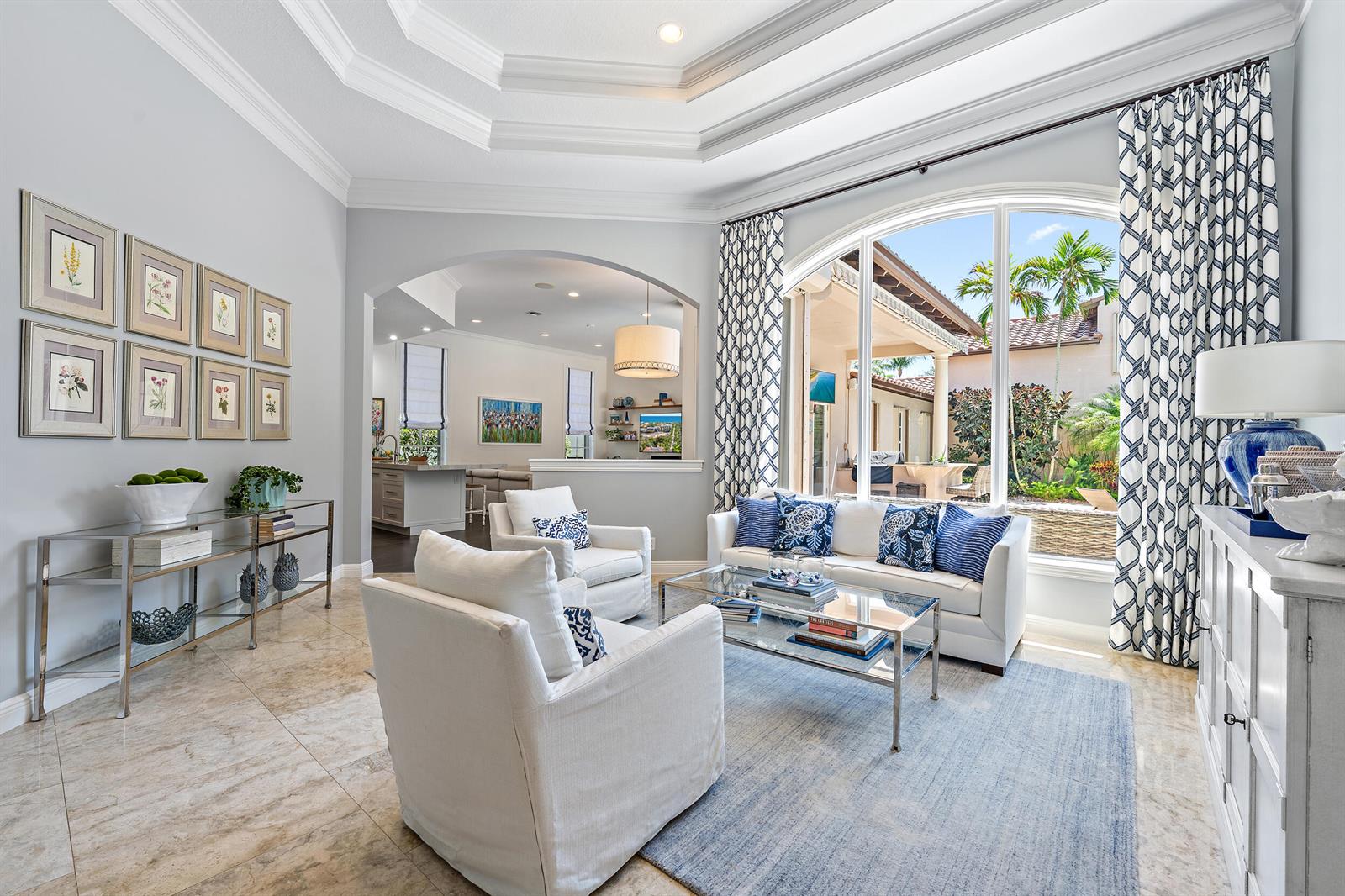 A bright living room features a tray ceiling, arched entryway, and large windows with patterned curtains — 105 Segovia Way, Jupiter FL 33458, JUPITER, FL