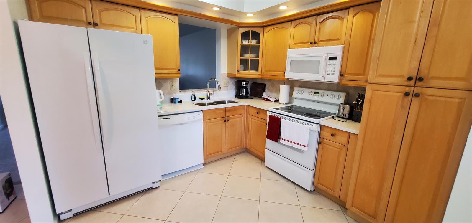 A kitchen features light wood cabinets, white appliances, and beige tile flooring — 260 NW 76th Avenue # 201, Margate FL 33063, MARGATE, FL