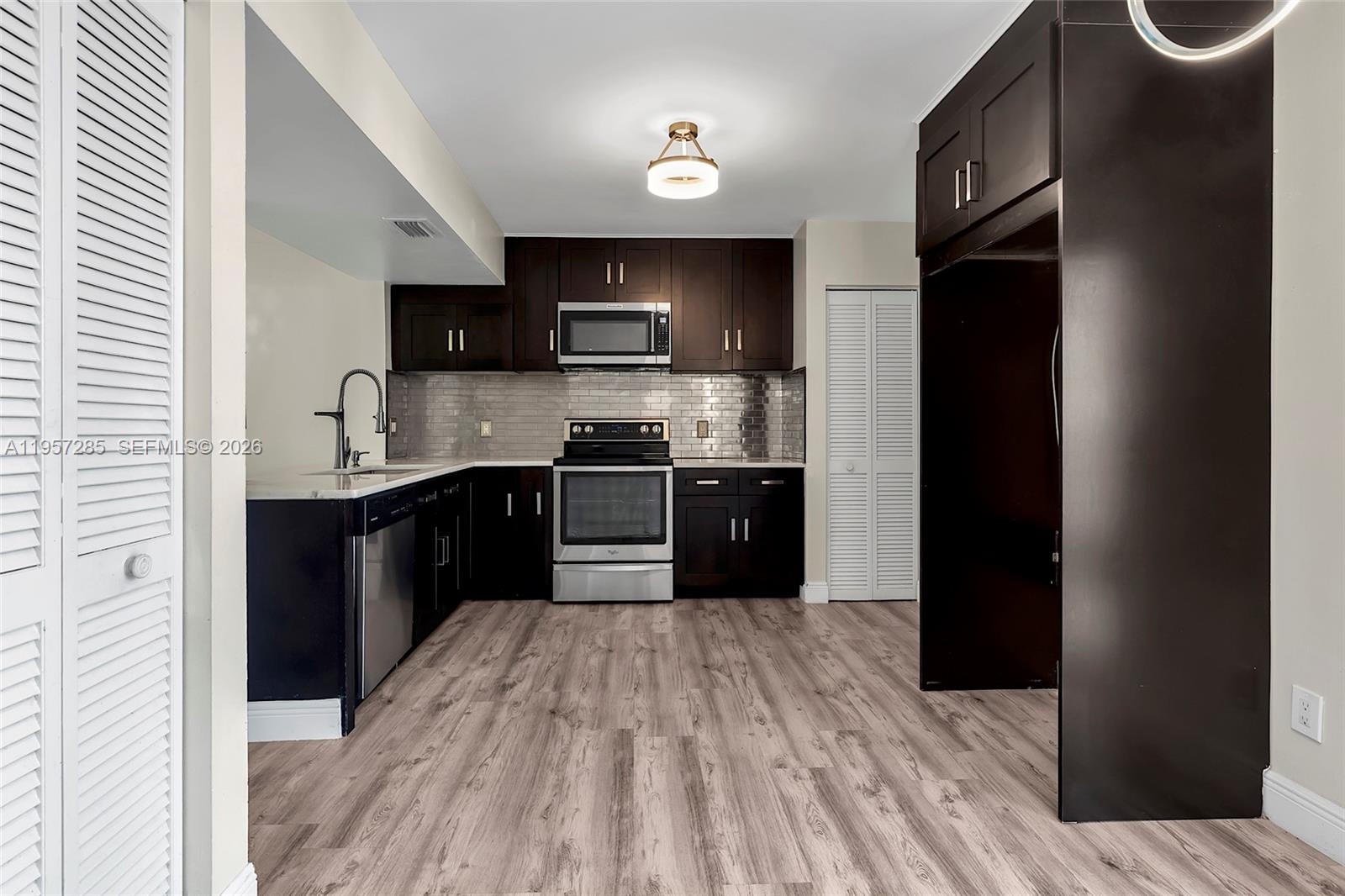 A kitchen features dark wood cabinets, stainless steel appliances, and light wood-look flooring — 6768 Canary Palm Cir, Boca Raton FL 33433, BOCA RATON, FL