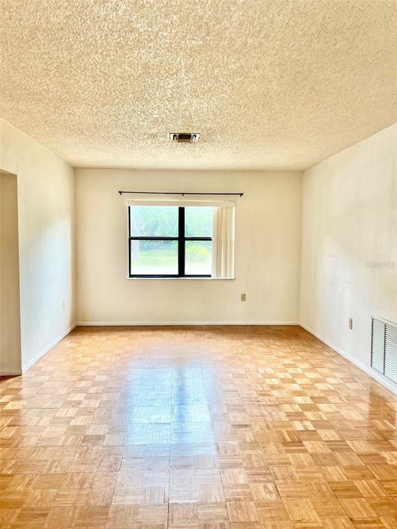 An empty room features light-colored walls, a textured ceiling, and a parquet wood floor — 718 BUCKMINSTER CIRCLE, ORLANDO, FL