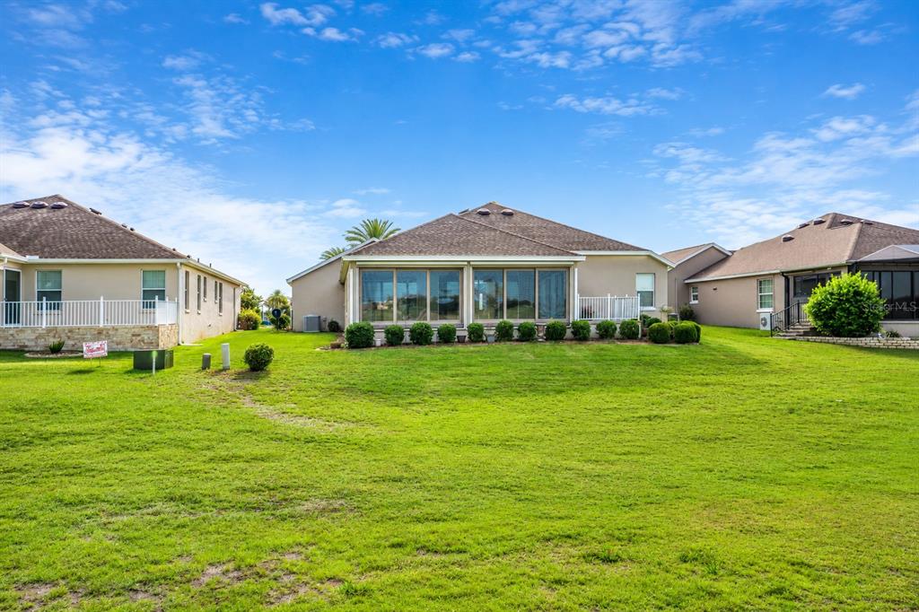 The rear exterior of a suburban house features a large screened-in lanai and grassy yard — 2696 MIDLAND TERRACE, THE VILLAGES, FL