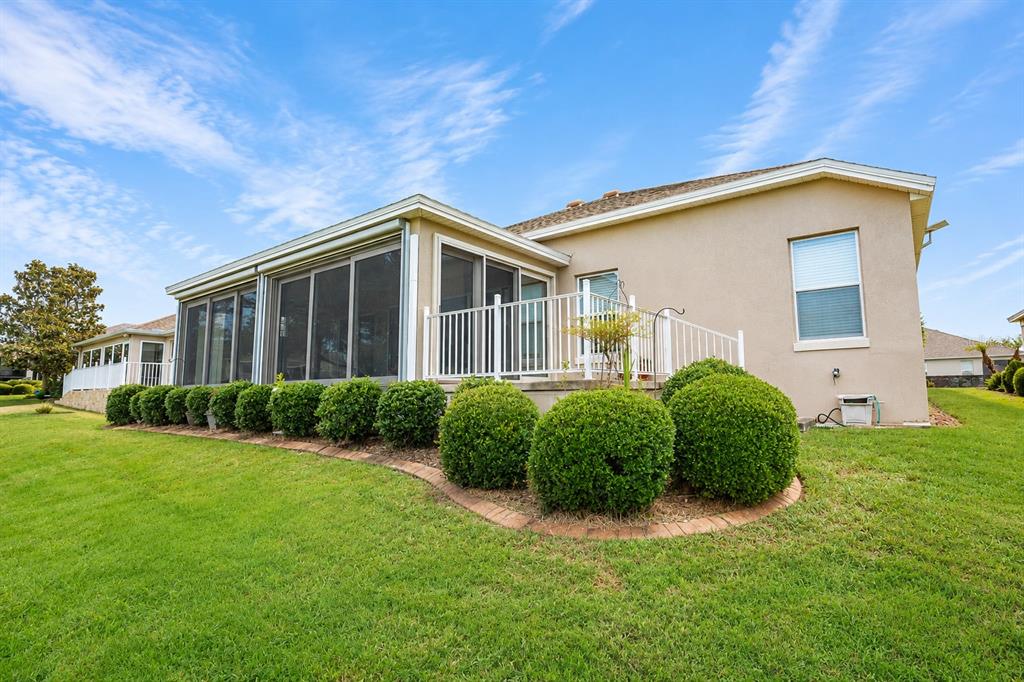 The exterior of a house features a screened-in porch, white railings, and manicured round shrubs — 2696 MIDLAND TERRACE, THE VILLAGES, FL