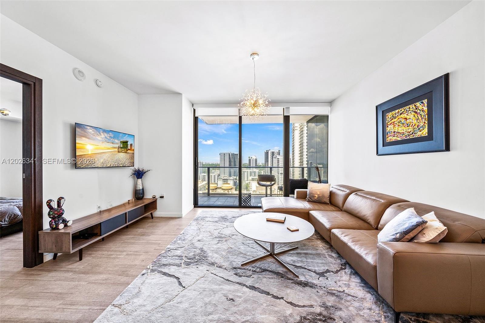A modern living room features a brown leather sectional, a patterned rug, and city views — 1000 Brickell Plz # 2111, Miami FL 33131, MIAMI, FL