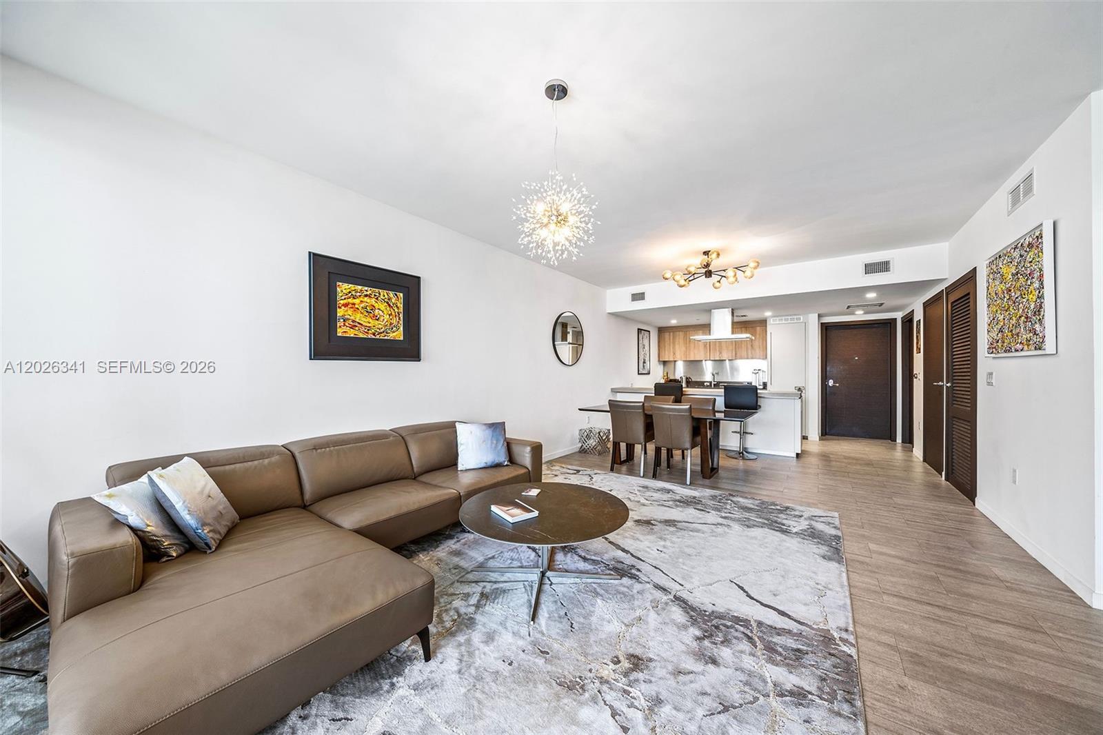 A modern living room features a brown sectional sofa, a round coffee table, and dining area — 1000 Brickell Plz # 2111, Miami FL 33131, MIAMI, FL