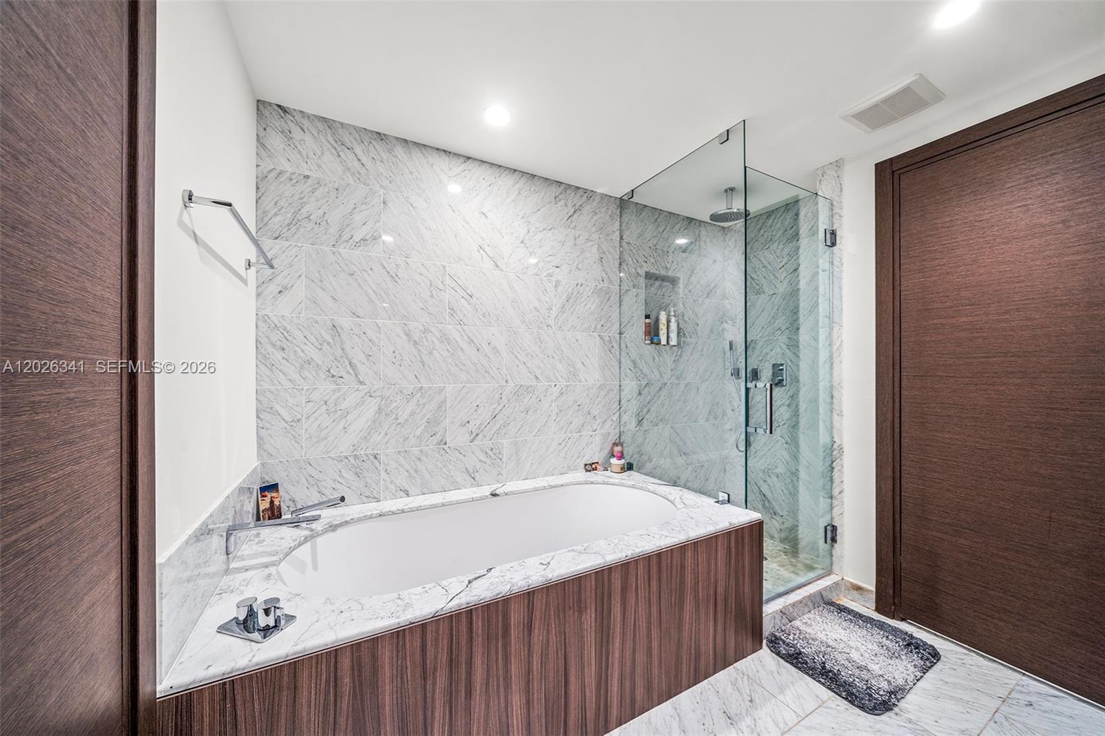 A modern bathroom features a marble-tiled soaking tub, a glass-enclosed shower, and wood-paneled accents — 1000 Brickell Plz # 2111, Miami FL 33131, MIAMI, FL