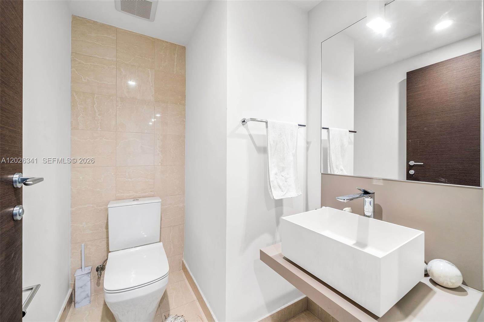 A modern bathroom features a white vessel sink, a wall-mounted toilet, and beige tile accents — 1000 Brickell Plz # 2111, Miami FL 33131, MIAMI, FL