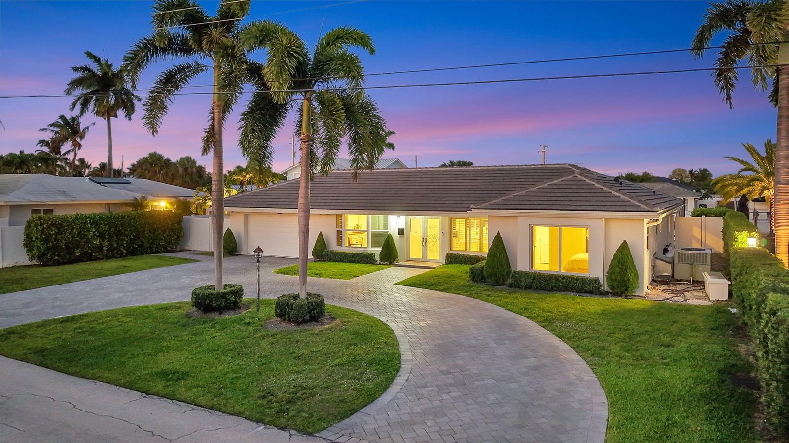 A single-story house with a paved driveway, palm trees, and a tiled roof at dusk — 4460 NE 26th Avenue, Lighthouse Point FL 33064, LIGHTHOUSE POINT, FL