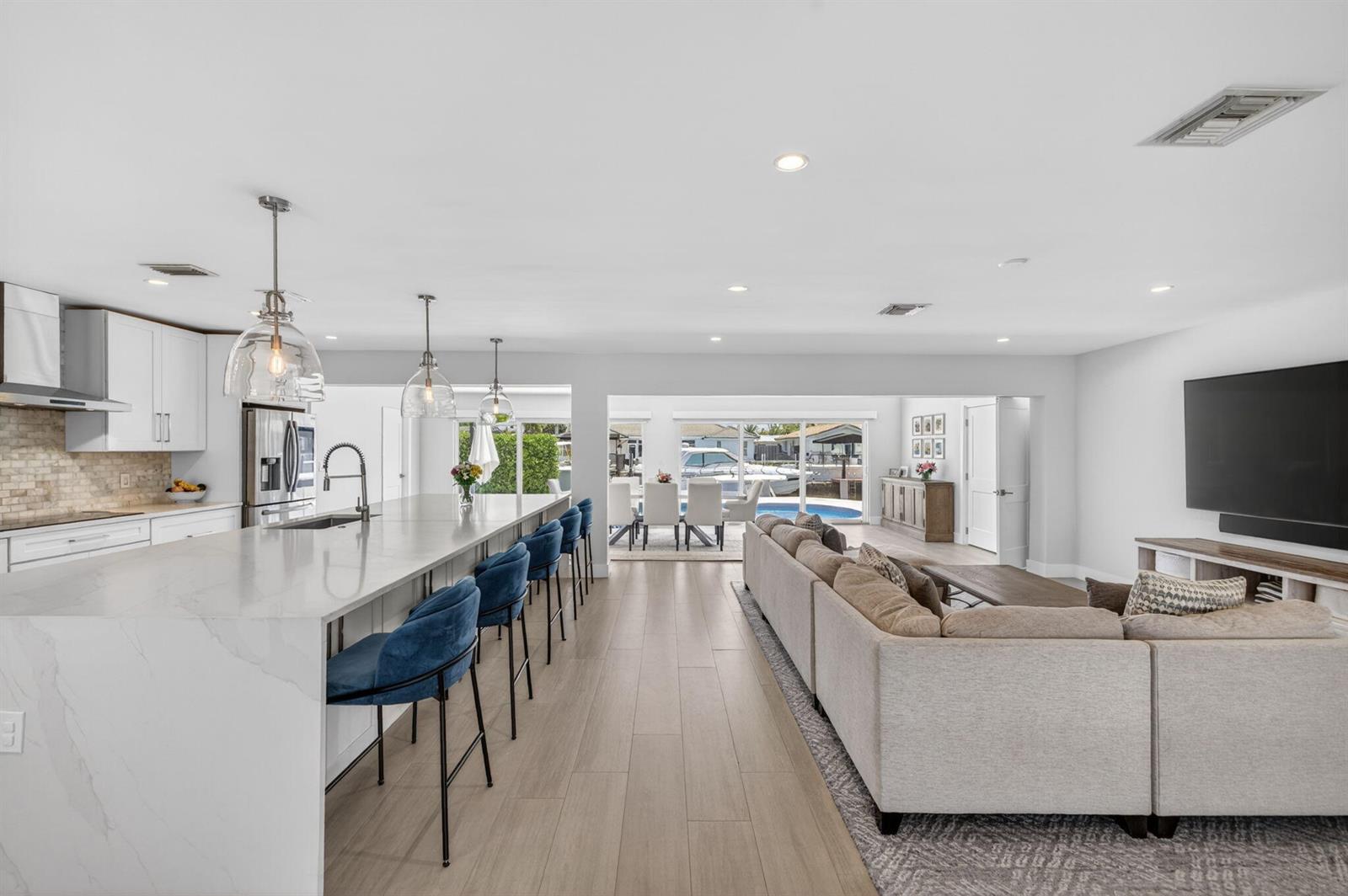 An open-concept kitchen and living area features a large marble island, blue stools, and sliding doors — 4460 NE 26th Avenue, Lighthouse Point FL 33064, LIGHTHOUSE POINT, FL