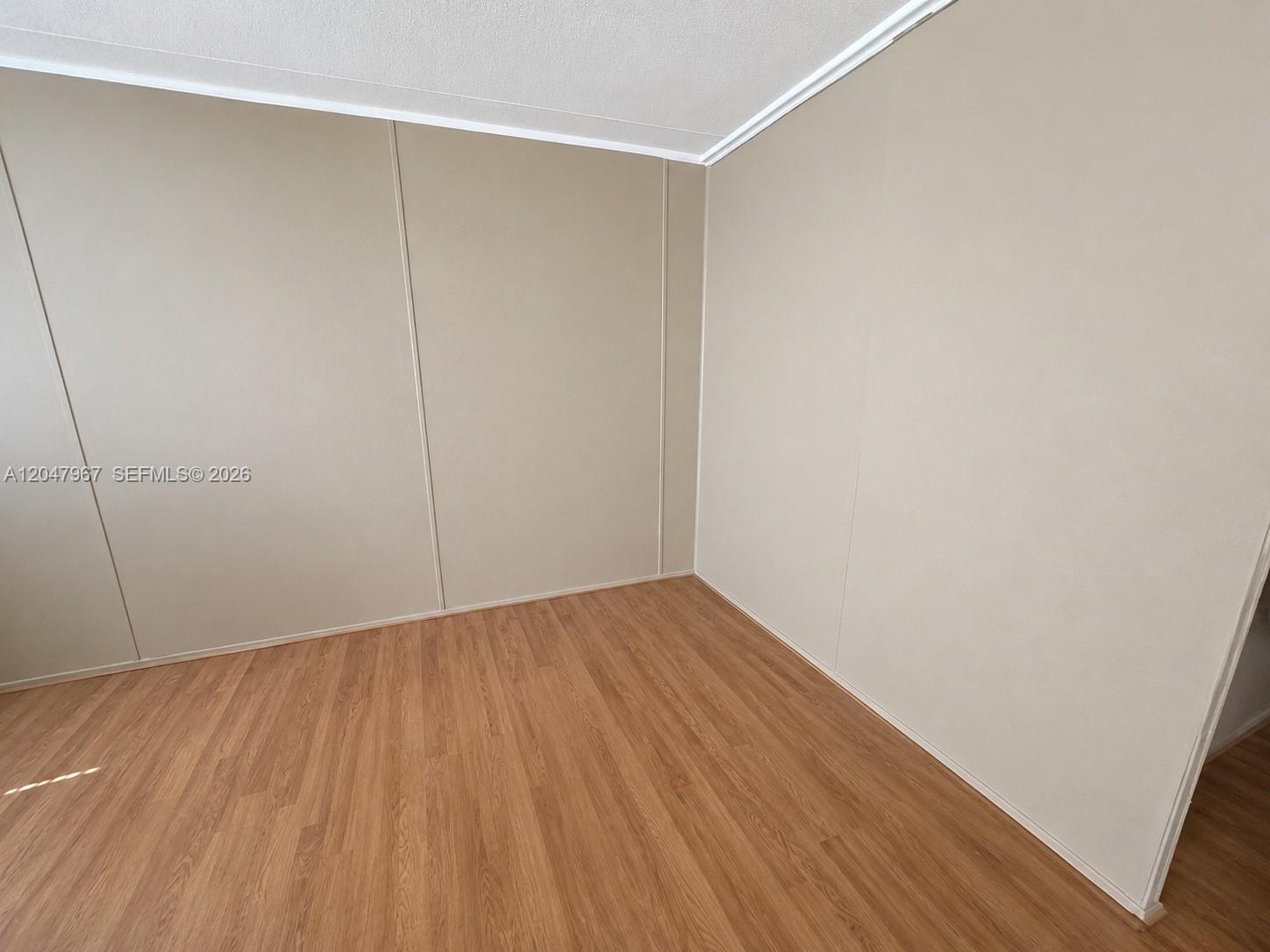 An empty room features light-colored paneled walls, white crown molding, and wood-look laminate flooring — 19800 SW 180th Ave Lot 583, Miami FL 33187, MIAMI, FL