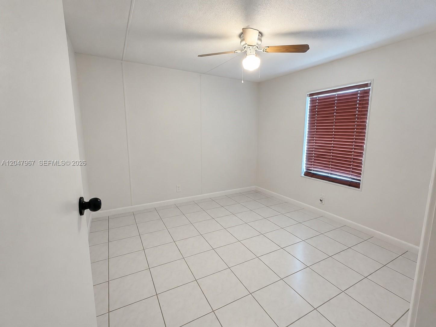 An empty bedroom features white walls, light-colored tile flooring, a ceiling fan, and a window — 19800 SW 180th Ave Lot 583, Miami FL 33187, MIAMI, FL