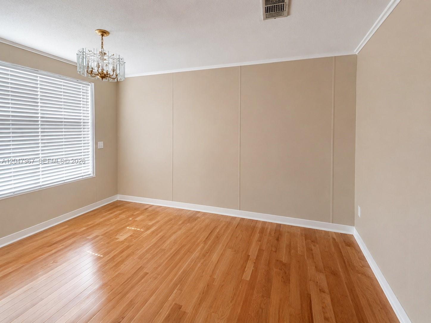 An empty room features light-colored panel walls, hardwood flooring, and a crystal chandelier — 19800 SW 180th Ave Lot 583, Miami FL 33187, MIAMI, FL