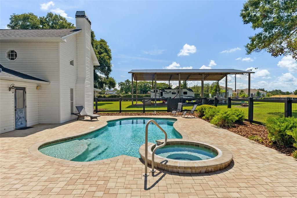 A backyard features a swimming pool, a raised spa, and a covered RV storage structure — 37714 FAIRFIELD LANE, DADE CITY, FL