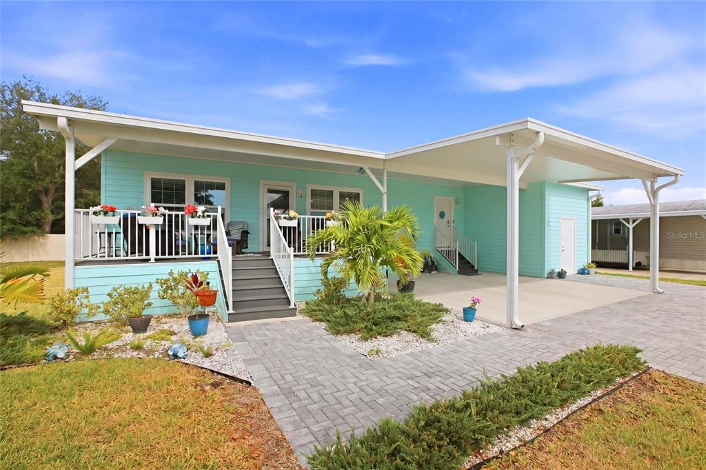 A light blue manufactured home features a covered porch, a carport, and a paved walkway — 4378 MANATEE LOOP UNIT 19A, PUNTA GORDA, FL