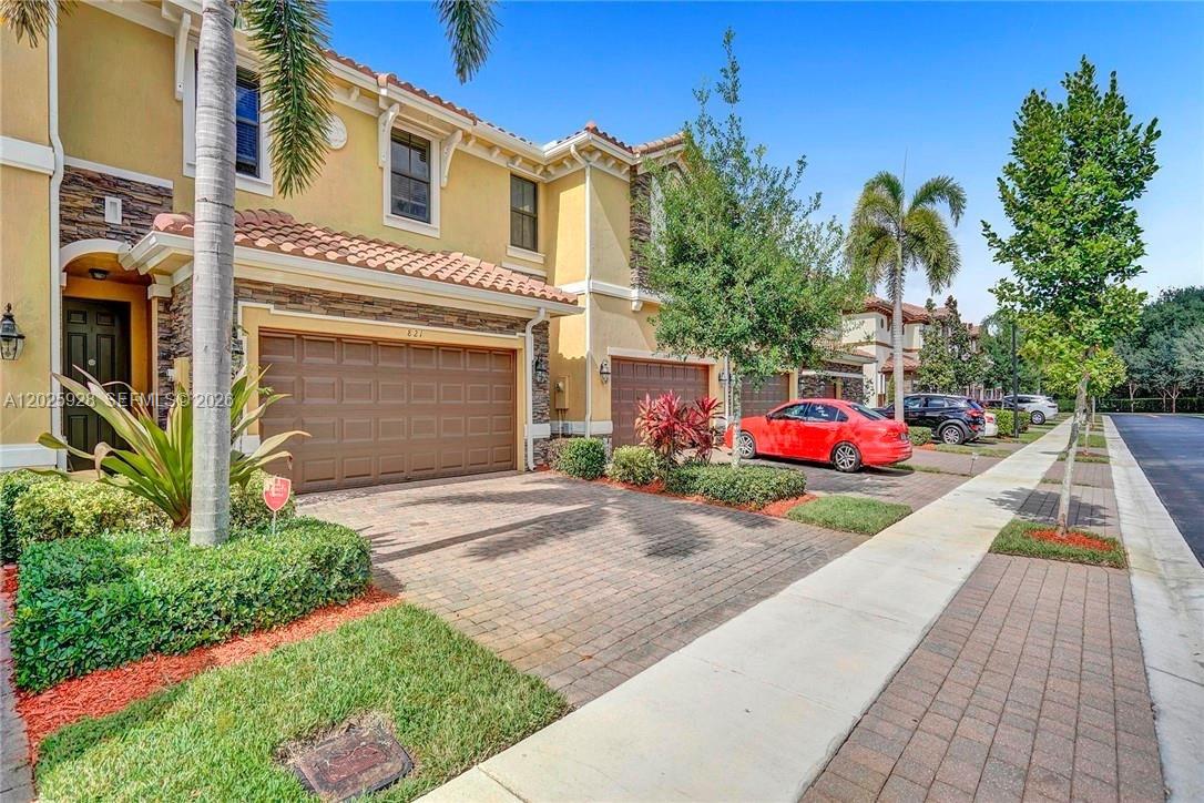 A two-story townhouse exterior features a paved driveway, a garage, and a small front lawn — 821 E Village Cir # 821, Davie FL 33325, DAVIE, FL