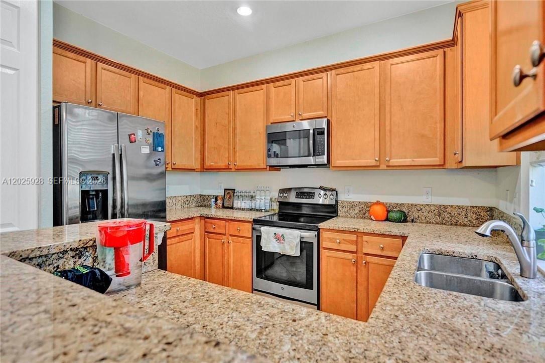 A kitchen features light wood cabinets, granite countertops, and stainless steel appliances — 821 E Village Cir # 821, Davie FL 33325, DAVIE, FL