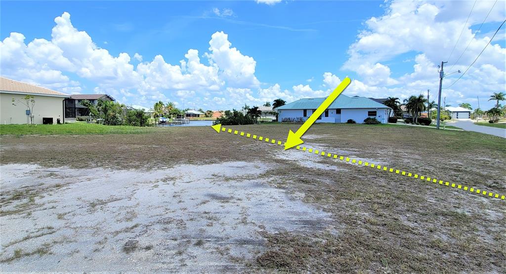A vacant, grassy residential lot with a yellow arrow and dashed line indicating property boundaries — 3690 WHIPPOORWILL BOULEVARD, PUNTA GORDA, FL