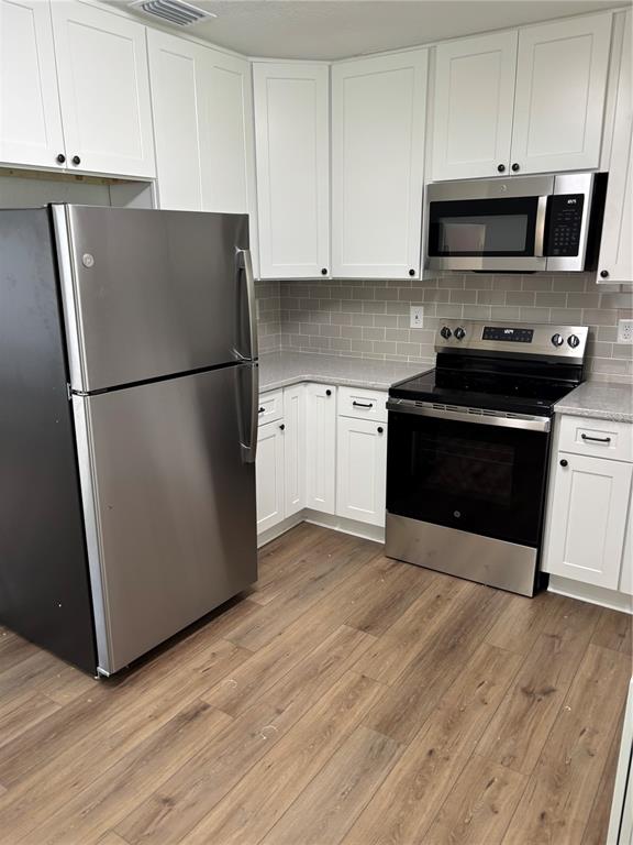 A kitchen features white cabinets, stainless steel appliances, gray tile backsplash, and wood-look flooring — 2716 HARDIN COMBEE ROAD, LAKELAND, FL