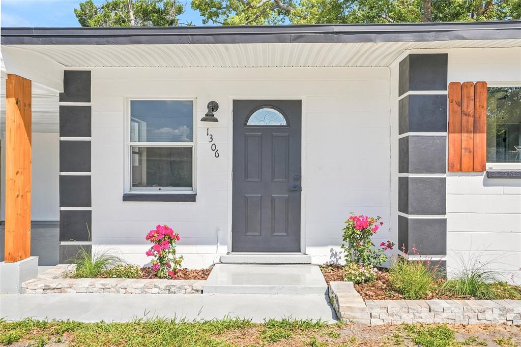 A white house exterior features a dark gray front door, black accents, and landscaping — 1306 DARTMOUTH DRIVE, BRADENTON, FL