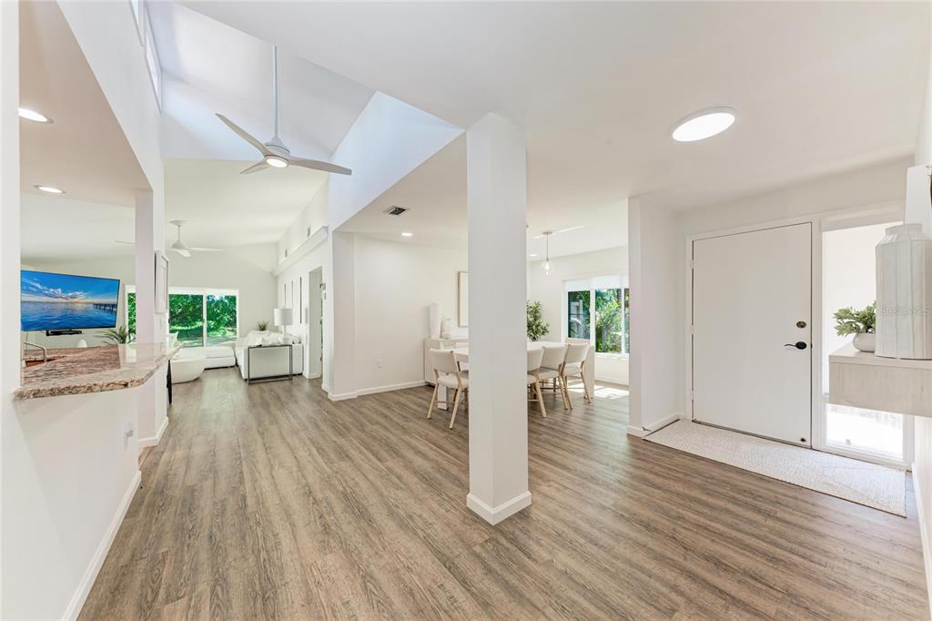 A bright, open-concept living and dining area features white walls, vaulted ceilings, and wood-look flooring — 6416 WOOD OWL CIRCLE, BRADENTON, FL