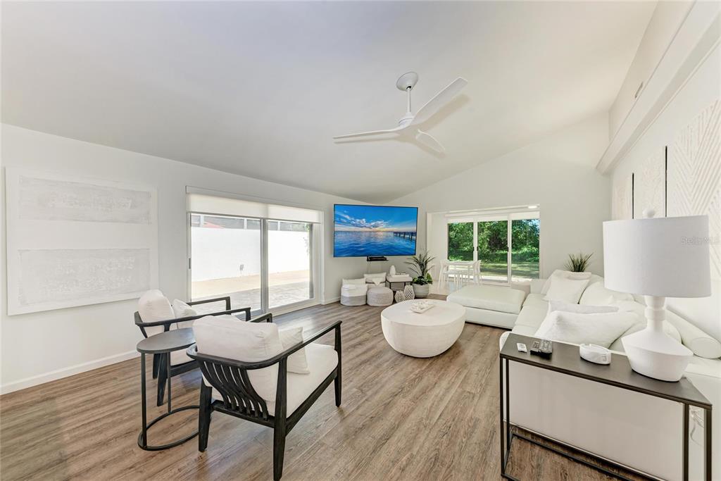 A bright living room features white furniture, a wall-mounted television, and wood-look flooring — 6416 WOOD OWL CIRCLE, BRADENTON, FL