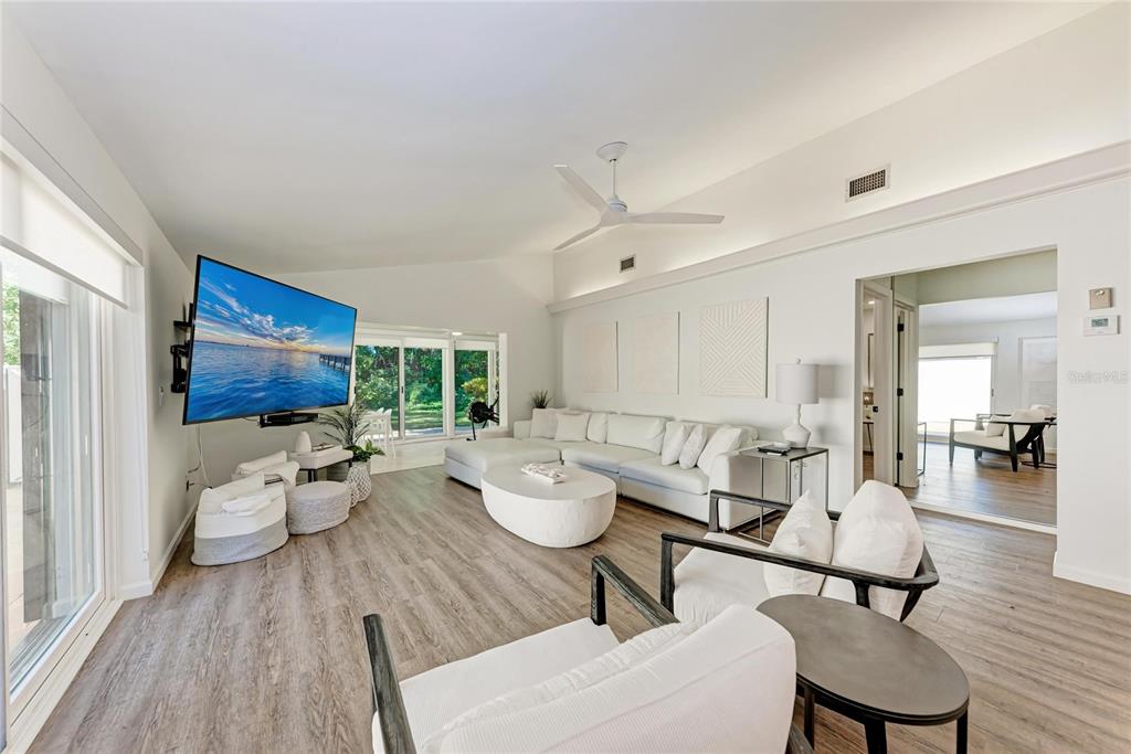 A bright living room features white furniture, a wall-mounted television, and wood-look flooring — 6416 WOOD OWL CIRCLE, BRADENTON, FL