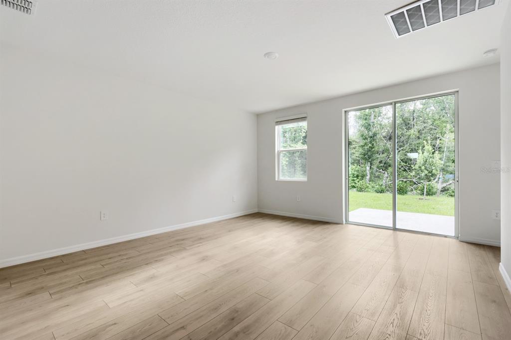 An empty room with light wood-look flooring, white walls, a window, and sliding glass doors — 7426 MIA VINE DRIVE, BROOKSVILLE, FL