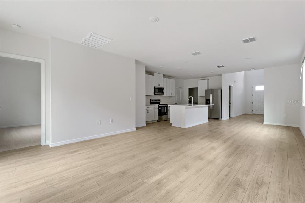 An open-concept living area features light wood-look flooring, white walls, and a modern kitchen — 7426 MIA VINE DRIVE, BROOKSVILLE, FL
