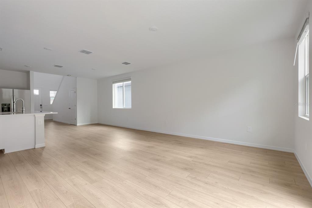 An open-concept living area features light wood-look flooring, white walls, and a kitchen island — 7426 MIA VINE DRIVE, BROOKSVILLE, FL