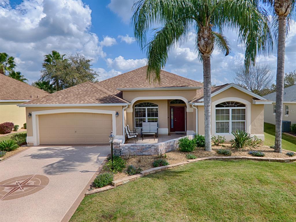 A single-story tan house with a two-car garage, stone accents, and a palm tree — 1979 REMBERT ROAD, THE VILLAGES, FL