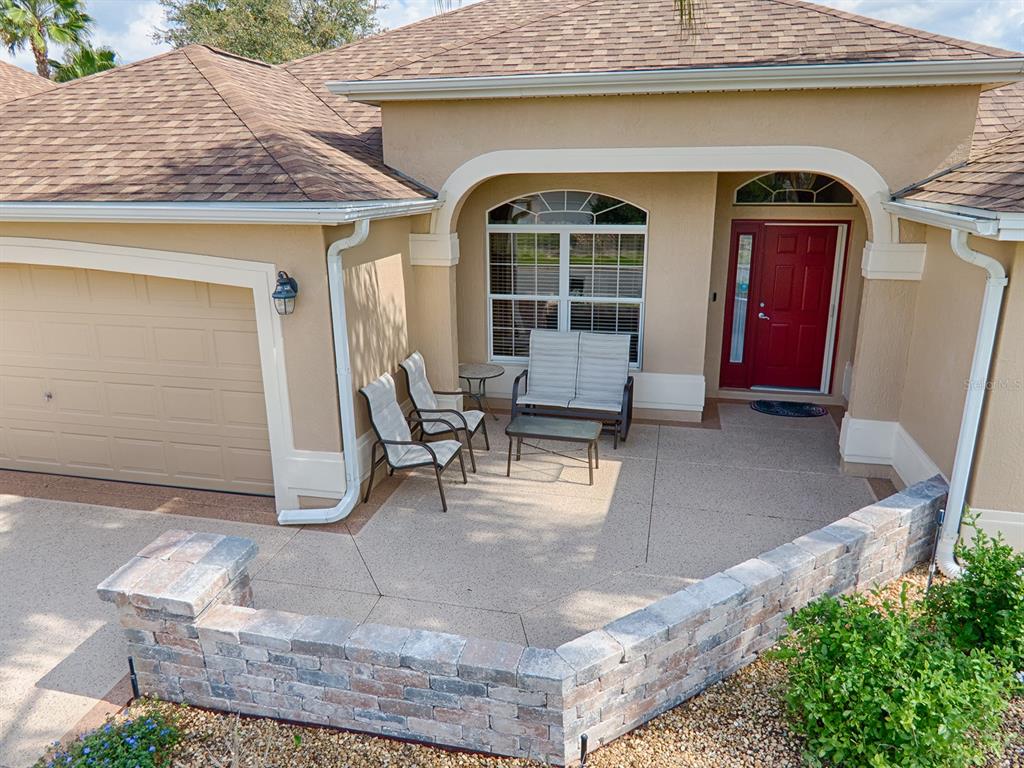 A tan house exterior features a red front door, a garage, and a paved patio — 1979 REMBERT ROAD, THE VILLAGES, FL
