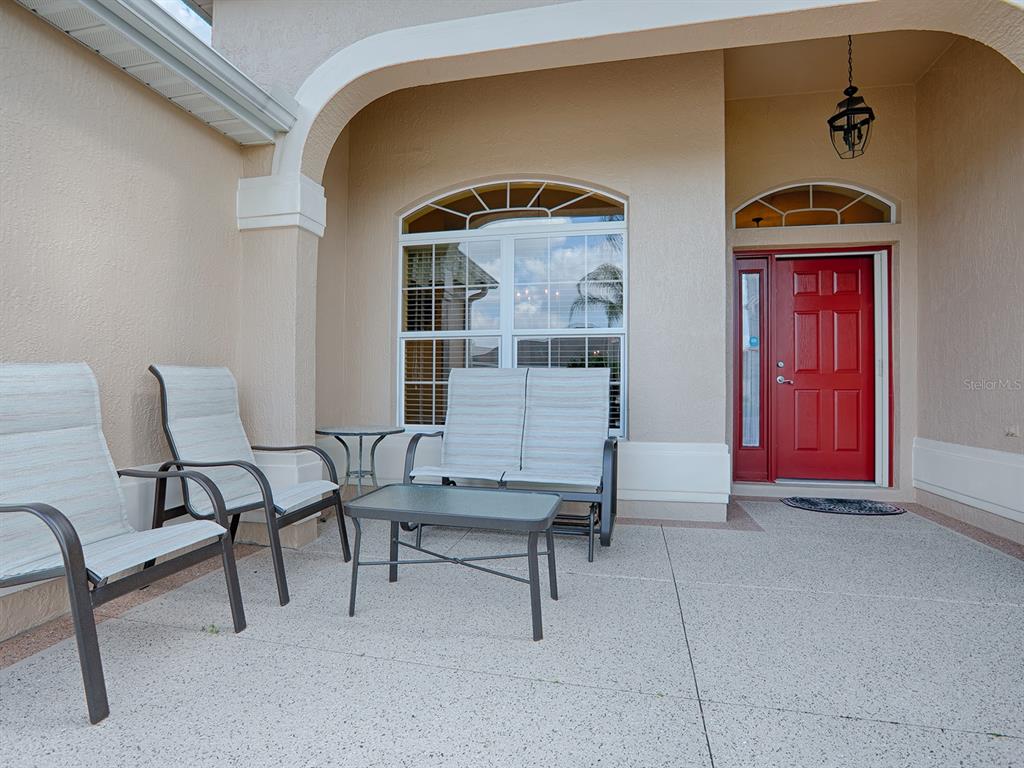 A covered front porch features a red door, a large window, and patio furniture — 1979 REMBERT ROAD, THE VILLAGES, FL