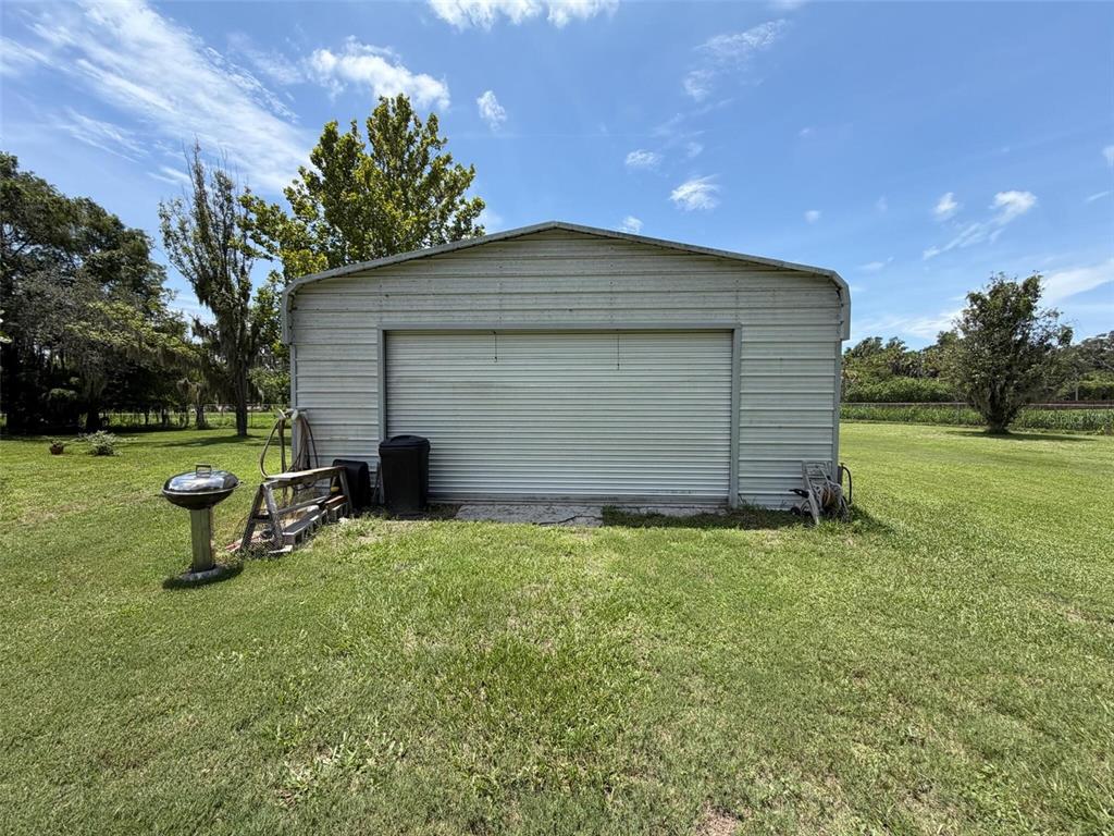 A detached metal garage sits in a grassy yard under a bright blue sky — 3707 36TH STREET E, BRADENTON, FL