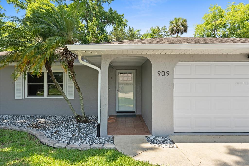 A gray house exterior features a white garage door, a covered entryway, and a palm tree — 909 BENTWOOD LANE UNIT 1, PORT ORANGE, FL