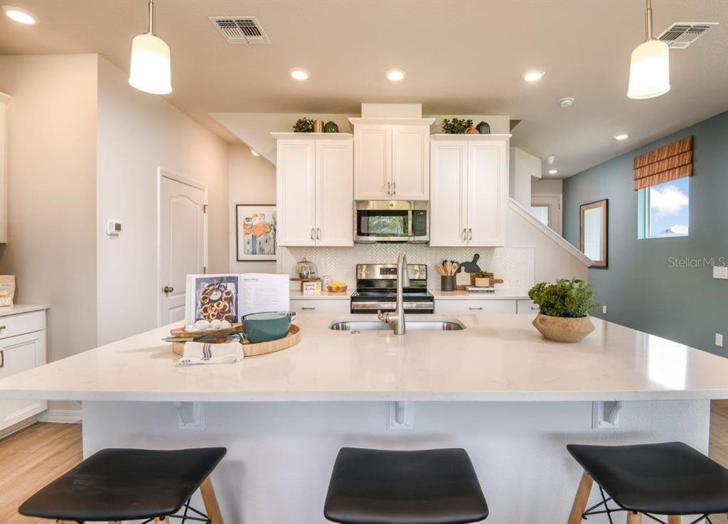 A kitchen features a large white quartz island, white cabinetry, and stainless steel appliances — 1789 TERRAPIN ROAD, OCOEE, FL