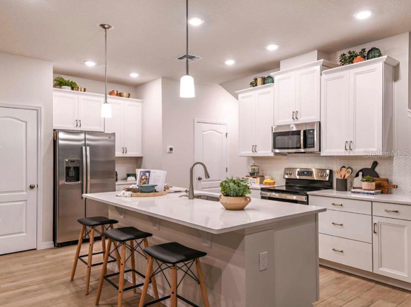 A modern kitchen features white cabinetry, stainless steel appliances, a central island, and bar stools — 1789 TERRAPIN ROAD, OCOEE, FL