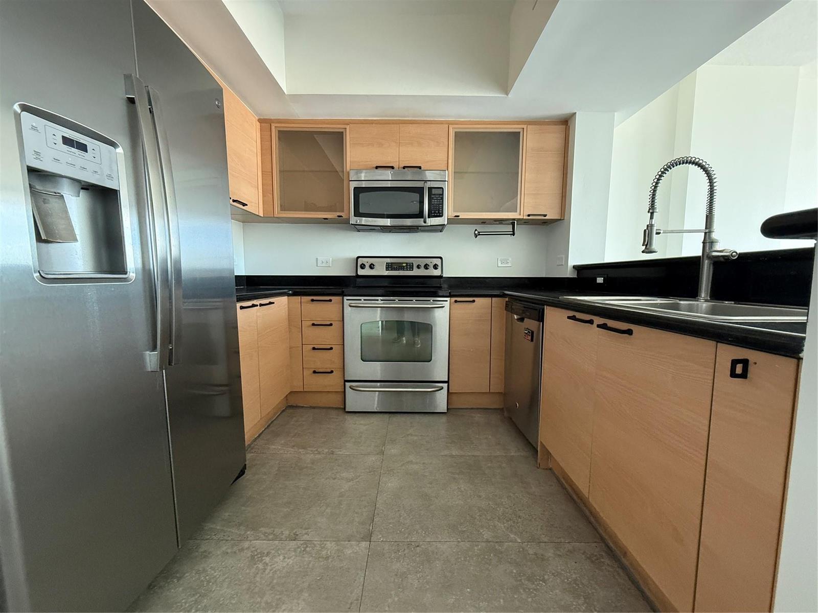 A kitchen features light wood cabinets, stainless steel appliances, and black countertops on tile flooring — 140 S Dixie Highway # 915, Hollywood FL 33020, HOLLYWOOD, FL