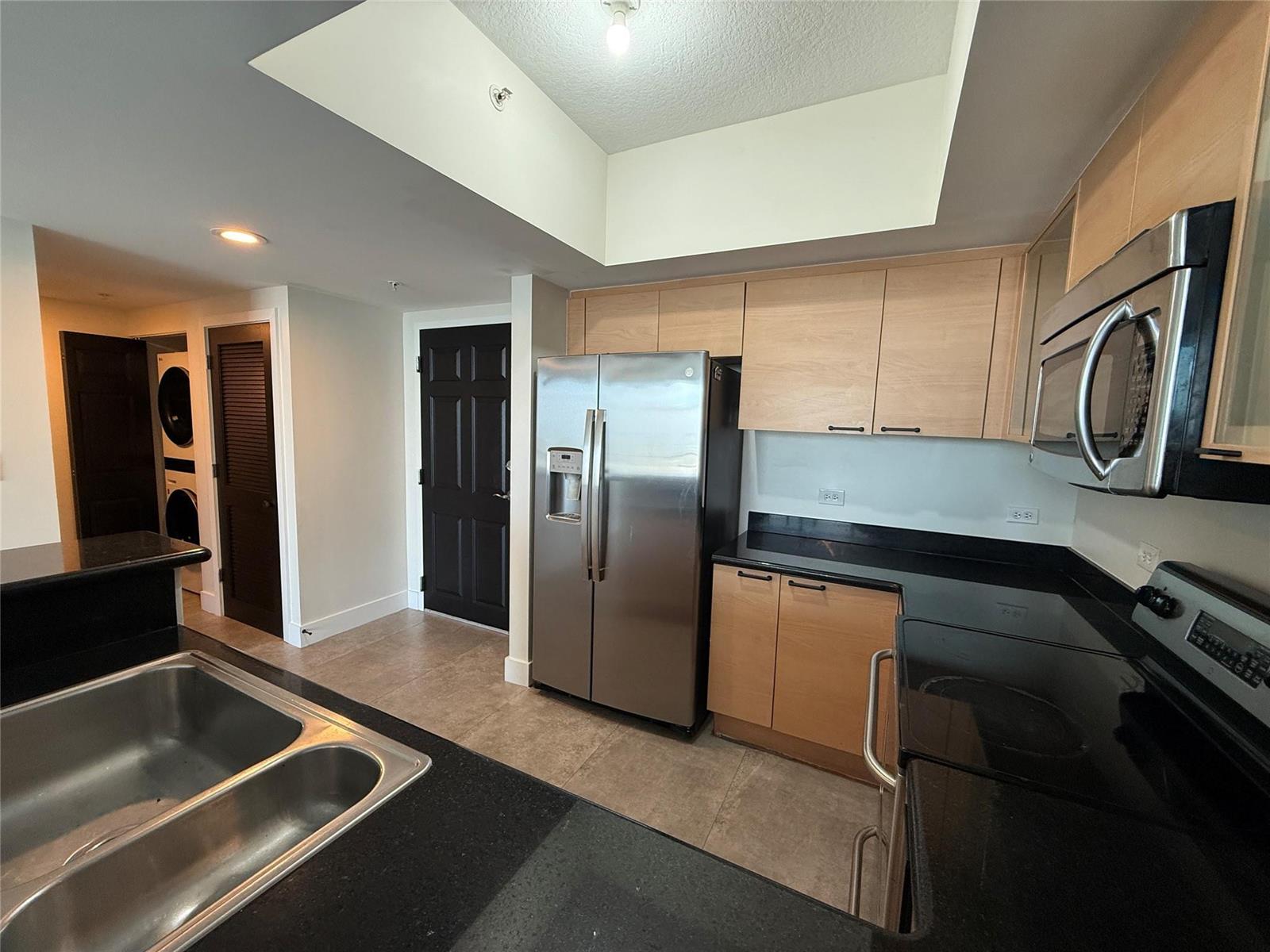A kitchen features light wood cabinets, black countertops, stainless steel appliances, and tile flooring — 140 S Dixie Highway # 915, Hollywood FL 33020, HOLLYWOOD, FL