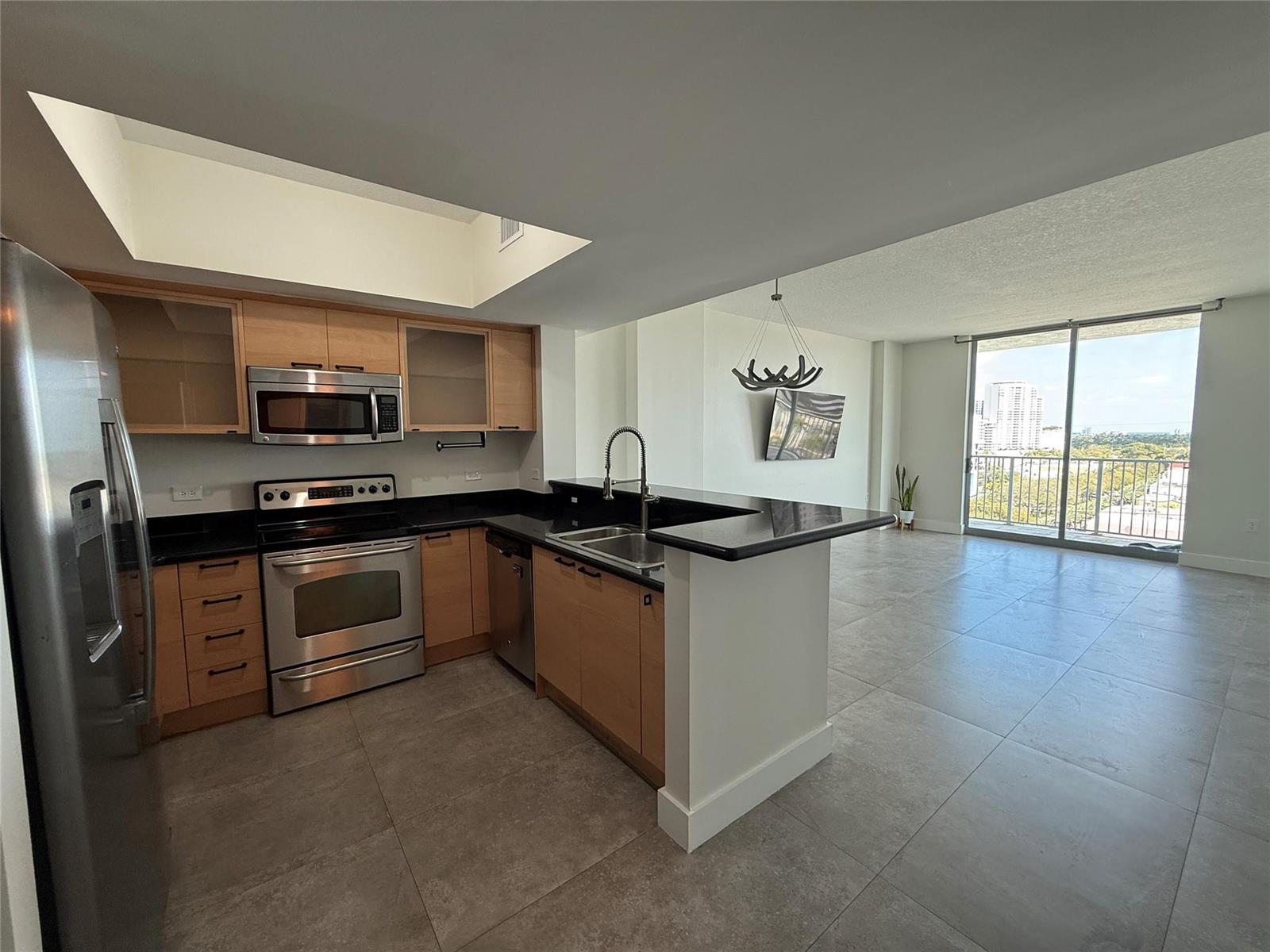 A kitchen with light wood cabinets and black countertops opens into a living area — 140 S Dixie Highway # 915, Hollywood FL 33020, HOLLYWOOD, FL