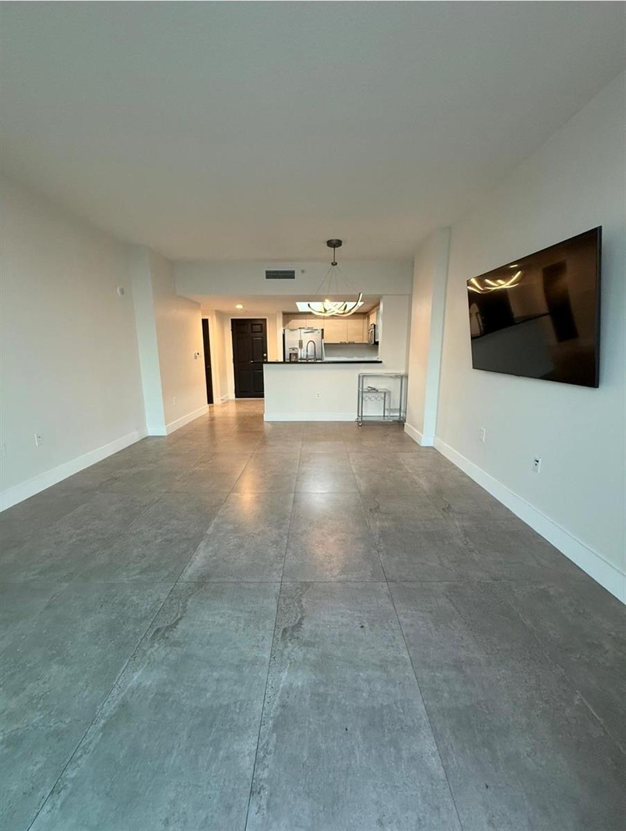 A living room with large gray floor tiles, white walls, and a mounted television — 140 S Dixie Highway # 915, Hollywood FL 33020, HOLLYWOOD, FL