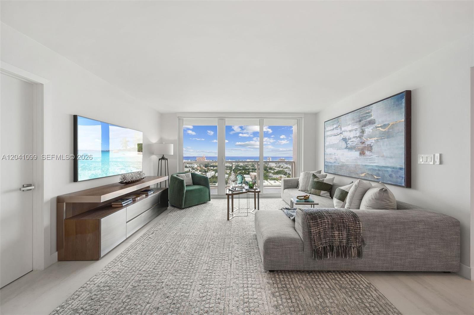 A modern living room features a grey sectional sofa, a green armchair, and ocean views — 650 West Ave # 1908, Miami Beach FL 33139, MIAMI BEACH, FL