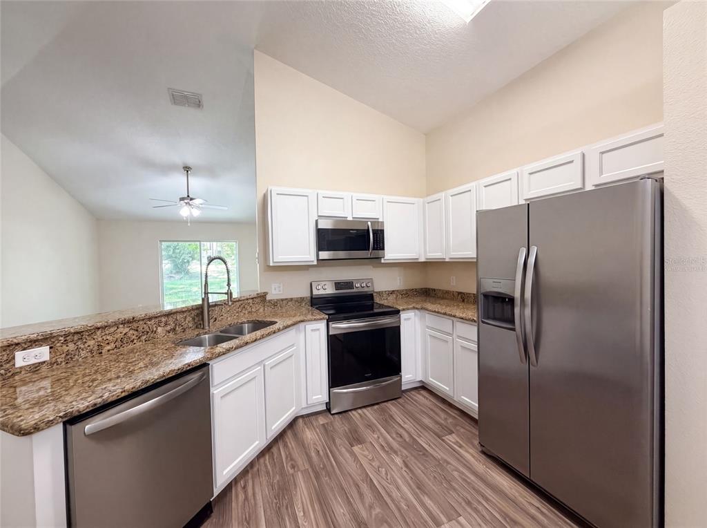 A kitchen features white cabinets, granite countertops, stainless steel appliances, and wood-look flooring — 33137 IRONGATE DRIVE, LEESBURG, FL