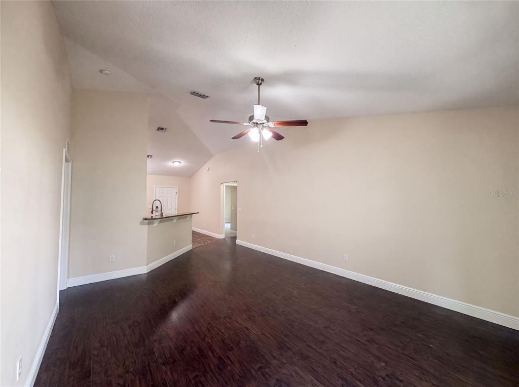 An empty living room features dark wood flooring, beige walls, and a vaulted ceiling — 33137 IRONGATE DRIVE, LEESBURG, FL