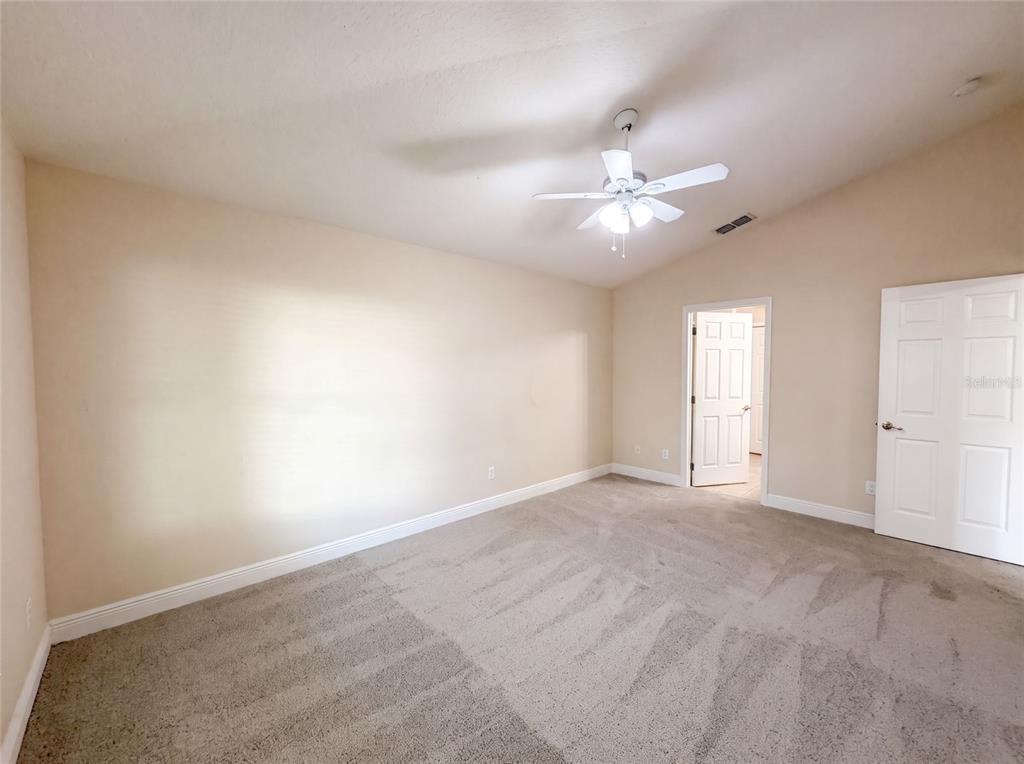 An empty bedroom features beige walls, carpeted flooring, a ceiling fan, and two white doors — 33137 IRONGATE DRIVE, LEESBURG, FL