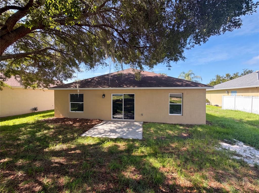 The rear exterior of a tan house features a concrete patio and a large tree — 33137 IRONGATE DRIVE, LEESBURG, FL